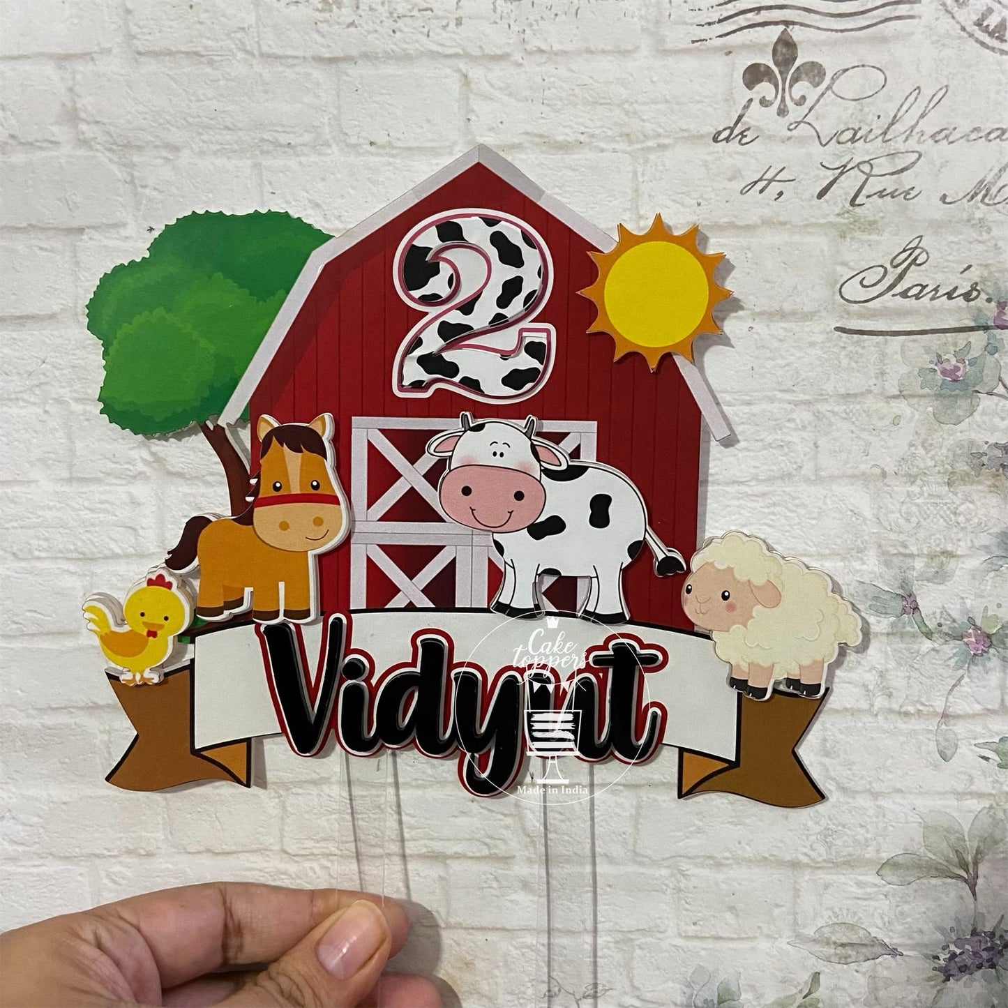 A customized cake topper featuring farm animals like a cow, pig, and chicken with a customised name tag.
